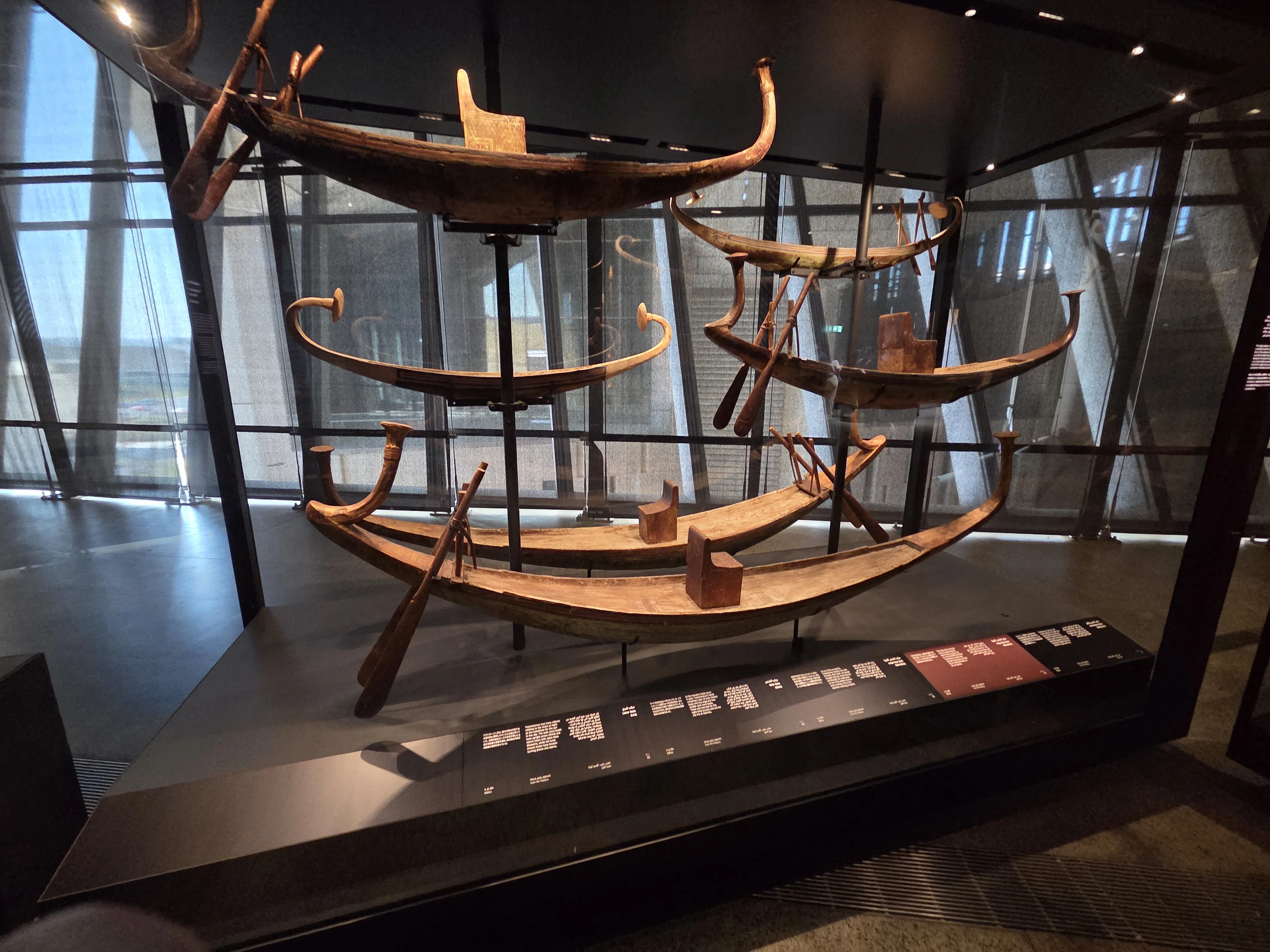 Bateaux funéraires en bois exposés dans une vitrine éclairée du Grand Musée Égyptien